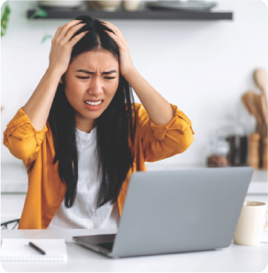 A person holding their head, frustrated, while at their computer due to their bad credit score.